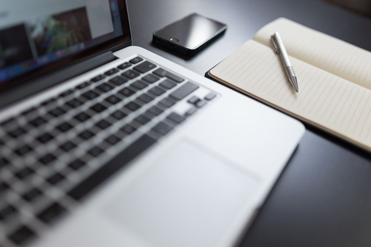 About Us A modern workspace featuring a laptop, notebook, smartphone, and pen on a desk.